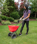 Woman using Deluxe Heavy-Duty Walk-Behind Commercial Broadcast Spreader With 80 Lb Capacity in a garden