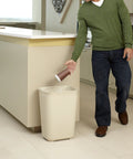 Person using Fire Resistant Wastebasket 40 Qt 10 Gal Beige For Hospitals Schools Hotels And Offices UL Certified Safety Trash Can Durable Resin With Textured Finish Built Tough in kitchen setting.