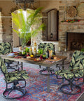 Outdoor dining area with tropical print chair cushions on swivel chairs, stone fireplace, and wooden table with decorative items.