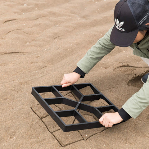 Person using 2 Pack Outdoor Pavement Molds For DIY Cement Stepping Stones Walkway Maker on sandy ground