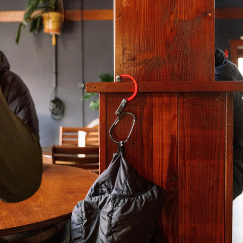 HeroClip Carabiner Gear Clip And Hook Medium holding bag on wood post in cafe environment.