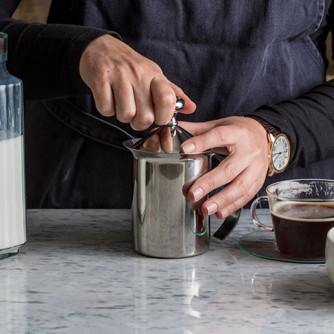 Handheld Milk Frother For Creamy Foam In Seconds, On The Go Stainless Steel Foamer used on a counter with coffee and milk