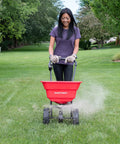 Deluxe Heavy-Duty Walk-Behind Commercial Broadcast Spreader With 80 Lb Capacity in use on a lawn, showing 10-inch poly tires and side spread control.