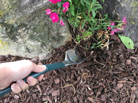 Person using Trake Garden Hand Tool Combo Trowel And Rake For Planting And Cultivating In Tight Spaces, digging near flowers.