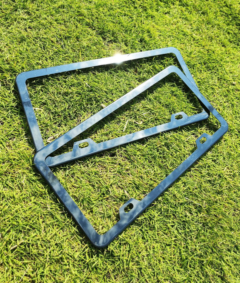 Dope Black Chrome Finish License Plate Frame Set on grass, featuring stainless steel construction and mirror finish, 2 Pack displayed.