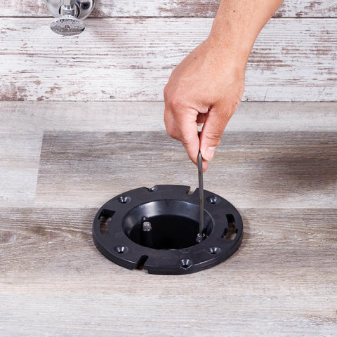 Hand installing 4-Inch ABS Cast Iron Closet Flange Replacement with Rubber Gasket and Stainless Steel Bolts on floor