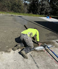 Worker wearing self supporting knee pads with removable shin guards, waterproof and washable, at construction site with concrete floor.