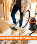 Man using Powerful 2 HP Wet Dry Vacuum With 4 Gallon Tank And Nozzles for cleanup in workshop, compact portable design, black and orange