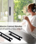 Woman sitting by window with tea and headphones, black self adhesive cabinet handles on window; 2 Pack Self Adhesive Cabinet Handles And Drawer Pulls