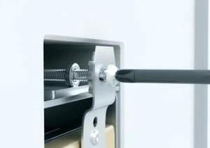 Close-up of an Adjustable Outlet Spacer 50pk being installed with a screwdriver, showing its metal and plastic components.