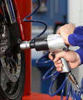 Person using pneumatic wrench on motorcycle wheel in workshop