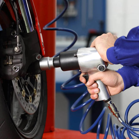 Person using pneumatic wrench on motorcycle wheel in workshop