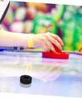 Air hockey table with player using a red paddle, black bumper shown on the table surface