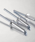 Close-up of three 250 Pack Aluminum Blind Rivets Three Sixteenths By One Half Inch With Aluminum Grip And Steel Mandrel on metal surface.