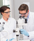 Scientists wearing ANSI Z87.1 Anti Fog Safety Goggles With Adjustable Frames working with a microscope in a lab environment.