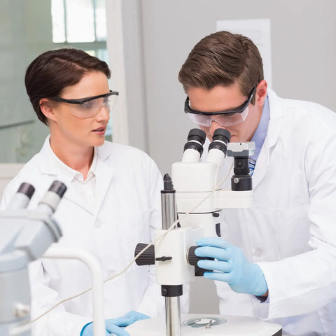 Scientists wearing ANSI Z87.1 Anti Fog Safety Goggles With Adjustable Frames working with a microscope in a lab environment.