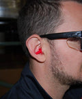 Man wearing ANSI Z87.1 Safety Glasses With Anti Fog UV Protection Clear Lens Side Shields indoors, showing side view with red earplugs.