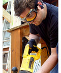Man wearing clear anti-fog safety goggles with ventilation channel and adjustable elastic strap using power tool on construction site.