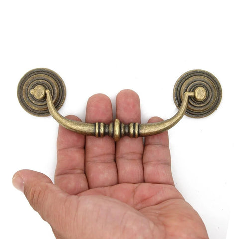 Hand holding Four Piece Vintage Antique Brass Bail Pull Handle Set For Wooden Drawers Cabinets And Cupboards showing design detail.