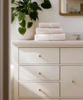 Bathroom cabinet with 30 Pack Antique Brass Cabinet Knobs 1-1/4 Inch Diameter Round Solid Zinc Alloy Drawer Pulls installed, plant on countertop.