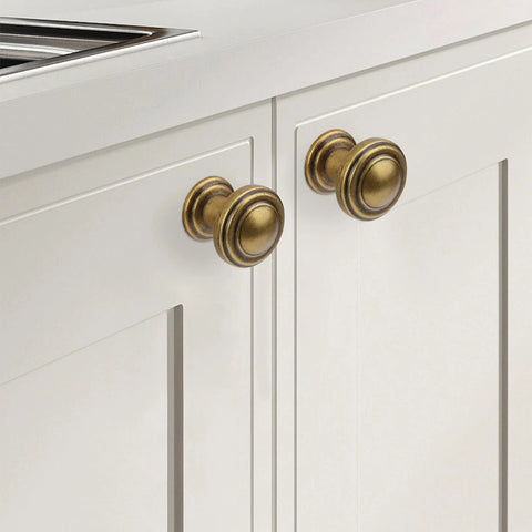Antique Brass Cabinet Knobs 10 Pack for kitchen cabinets, installed on white cabinet doors, showing its classic finish and durable construction.