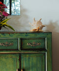Green cabinet with Antique Brass Drop Bail Drawer Pulls Six Pack With Two And A Half Inch Hole Centers, flowers, and seashell on top.