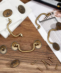 Vintage Bail Pull Handles Set Of 4 Antique Bronze Alloy Drop Pulls on wooden surface with screws, ideal for cabinets and dressers.