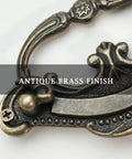 Close-up of antique brass finish on Baroque style drop bail drawer pull for classic furniture restoration.