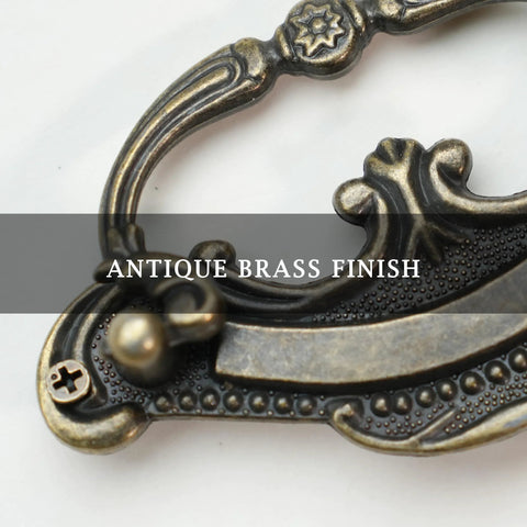 Close-up of antique brass finish on Baroque style drop bail drawer pull for classic furniture restoration.