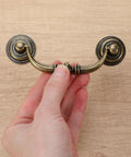 Hand holding vintage bronze drawer pull, part of a Set Of 10 Antique Drop Bail Pulls With 3.5 Inch Center Hole, 4.5 Inch total length