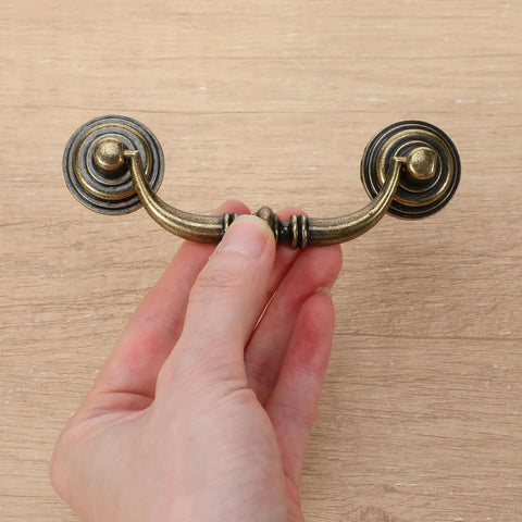 Hand holding vintage bronze drawer pull, part of a Set Of 10 Antique Drop Bail Pulls With 3.5 Inch Center Hole, 4.5 Inch total length