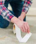 Person installing Heavy Duty Double Sided Tape For Carpet Tiles And Vinyl Flooring, ideal for artificial grass and gym tiles.