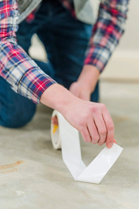 Person installing Heavy Duty Double Sided Tape For Carpet Tiles And Vinyl Flooring, ideal for artificial grass and gym tiles.