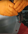 Mechanic applying Ultra Black Maximum Oil Resistant RTV Silicone Gasket Maker 9.5 Oz to metal surface with gloves.