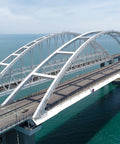 White steel arch bridge over turquoise water, elevated road deck with metal truss supports