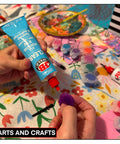 Person using a blue adhesive tube for arts and crafts with colorful materials and supplies around.