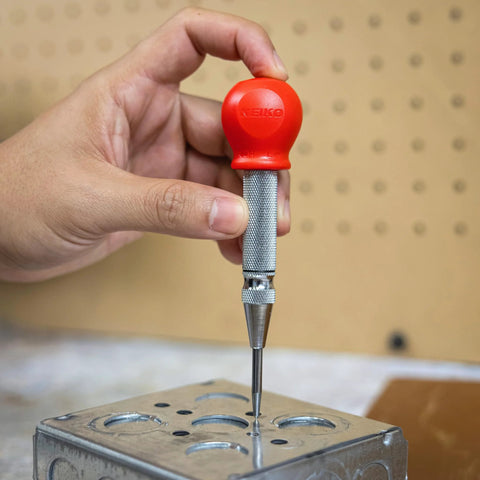 Hand holding 5-Inch Automatic Center Punch for Metal and Other Materials, demonstrating precision marking on metal surface.
