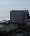Premium Sling Bag For Avata 2 FPV Drone With Multiple Internal Compartments beside Avata 2 drone on rocky surface
