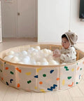 Baby playing in beige ball pit with 100 Ball Pit Balls Phthalate Free BPA Free Crush Proof Plastic in colorful playroom setting.