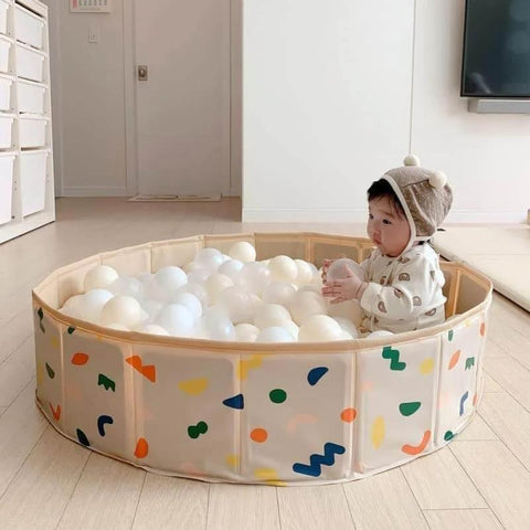 Baby playing in beige ball pit with 100 Ball Pit Balls Phthalate Free BPA Free Crush Proof Plastic in colorful playroom setting.