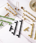 Various styles of bamboo-inspired cabinet pulls in gold, green, and black, arranged on a marble surface with decorative elements.