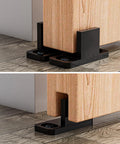 4 Pieces Barn Door Floor Guide Set For Sliding Closet Doors POM Plastic Bottom Track Guide Wall Mounted Adjustable For Grooved And Non Grooved Doors Includes Bypass Pocket And Screws Matte Black installed view showing black guides under wooden barn doors.