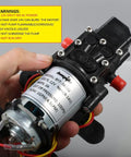 Person holding bayite 12V DC Fresh Water Pressure Diaphragm Pump with Hose Clamps Self Priming Sprayer Pump with Pressure Switch