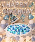 Birthday party setup with ball pit filled with blue, white, and green balls; "Happy Birthday" balloons and decorations surround the scene.