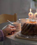 90th birthday cake with candles on table, hand holding a floral teacup