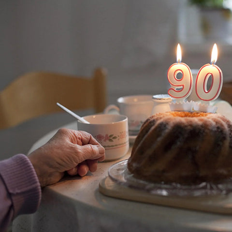 90th birthday cake with candles on table, hand holding a floral teacup
