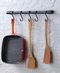 Kitchen Utensil Rack with Removable S Hook for Hanging Pots and Pans, Rod Hooks for Mugs, Wall Mounted Kitchen Rail Organizer, Aluminum,(Black-5 Hooks) displaying a pan and wooden utensils on a stone wall