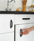 Hand reaching for 12 Pack Black Barn Door Handles 5.8 Inch Aluminum Alloy Cabinet Pulls on white kitchen cabinets