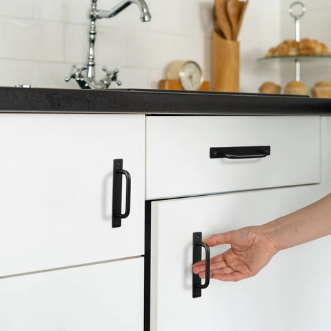 Hand reaching for 12 Pack Black Barn Door Handles 5.8 Inch Aluminum Alloy Cabinet Pulls on white kitchen cabinets