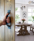 Person holding 9 Inch Sliding Barn Door Handle Set In Black For Interior And Exterior Doors on wooden door, showcasing installation.